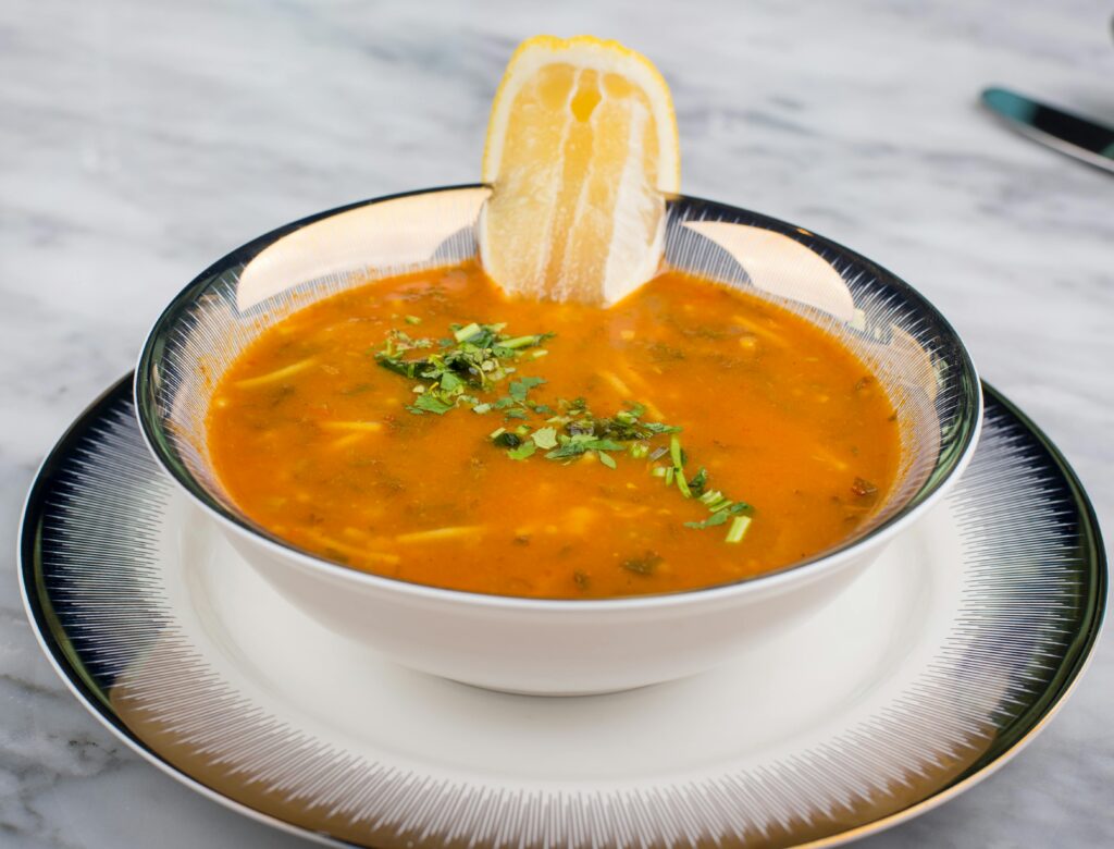Rich orange soup garnished with fresh herbs and lemon slice in an elegant bowl setting.